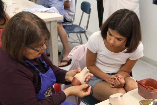 Image of Pueblo potter Maxine Toya showing a student how to polish a red slipped pot.