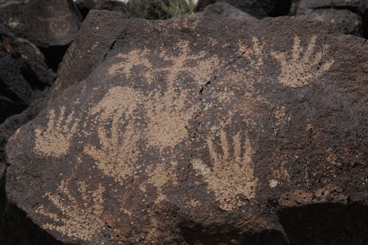 Image of human hand petroglyphs carved on dark volcanic rock at Petroglyph National Monument, New Mexico.