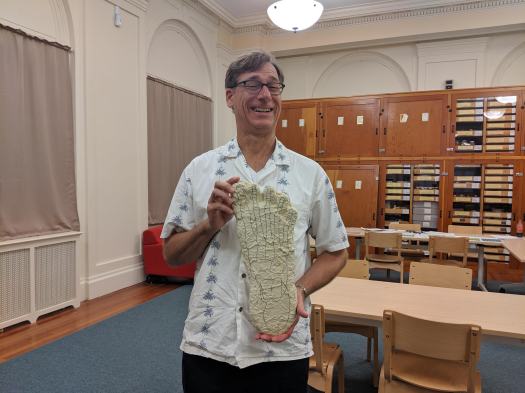 Ryan Wheeler, a tall man with glasses and a white Hawaiian style shirt folds the very large cast of a foot, said to be Bigfoot, a cryptid. The relative position of the foot bones has been marked by the late Bigfoot researcher Dr. Grover Krantz.