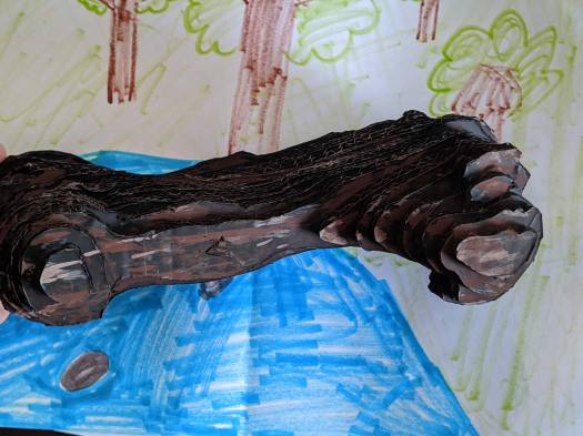 Image of the cardboard Megalonyx femur on a blue and green painted background.