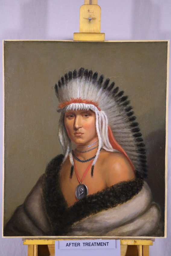 Image of cleaned oil painting showing Native American man with eagle feather headdress, silver peace medal necklace, and fur robes.