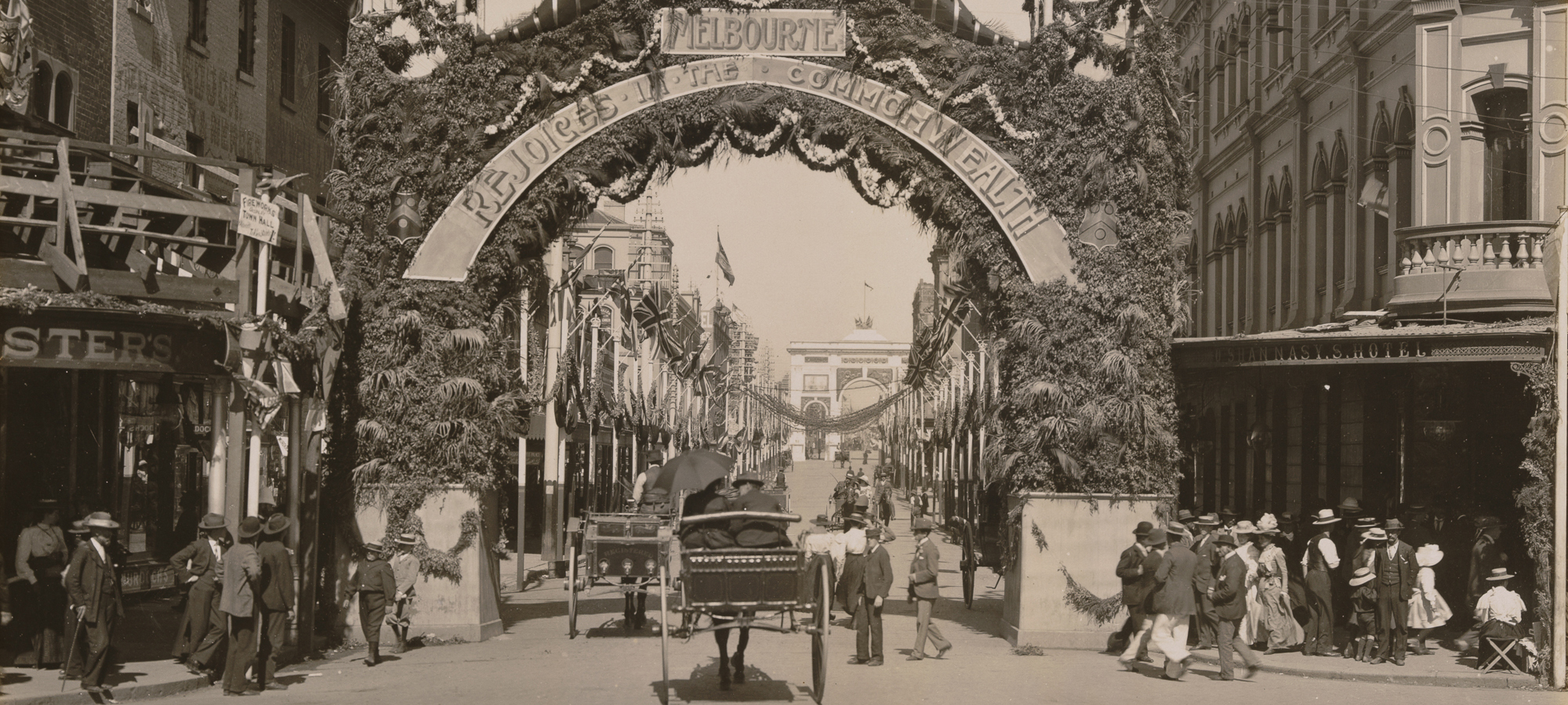 Street in Melbourne decorated with flags and garlands, with giant arch stretching across road and reading "Melbourne Rejoices in the Commonwealth".